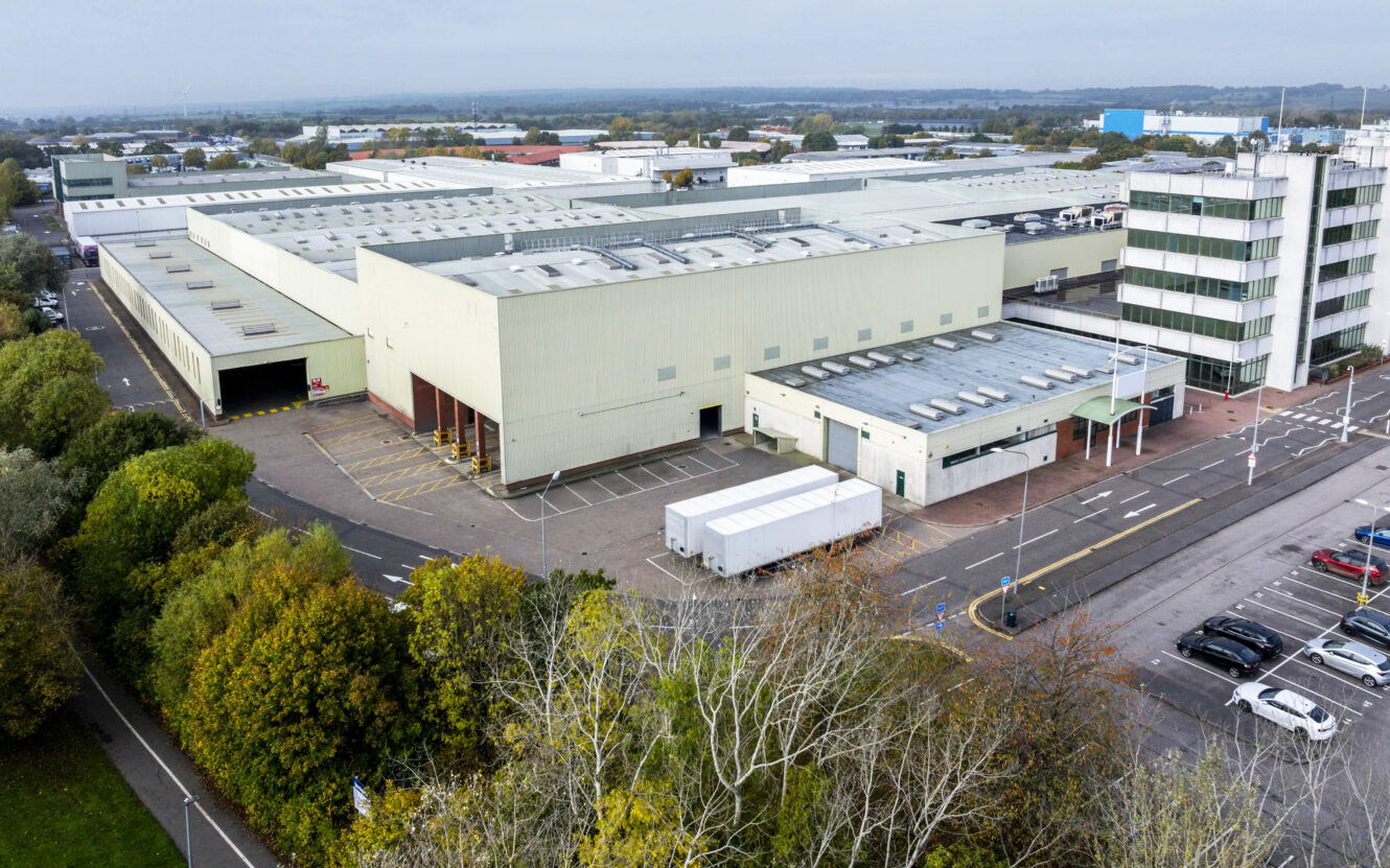 Aerial view of a large industrial warehouse and office building complex with adjacent parking lot and surrounding roads.