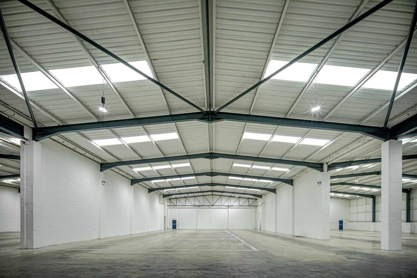 Interior of an empty, modern warehouse with white walls, high ceilings, exposed metal beams, and skylights letting in natural light.