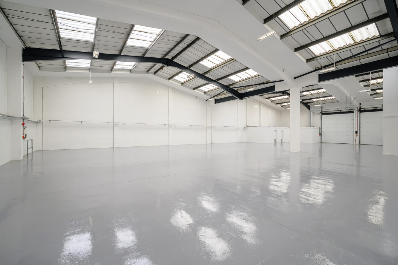Large, empty industrial warehouse with white walls, high ceilings, skylights, and polished concrete floors.