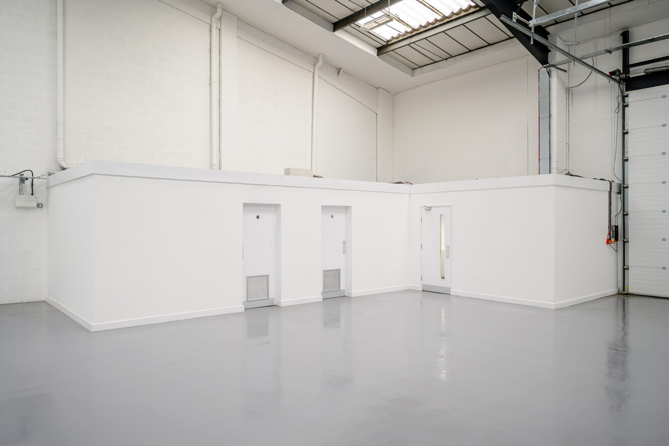 Industrial warehouse interior with clean white walls, three closed doors, polished gray concrete floor, high ceiling, and visible overhead lighting.