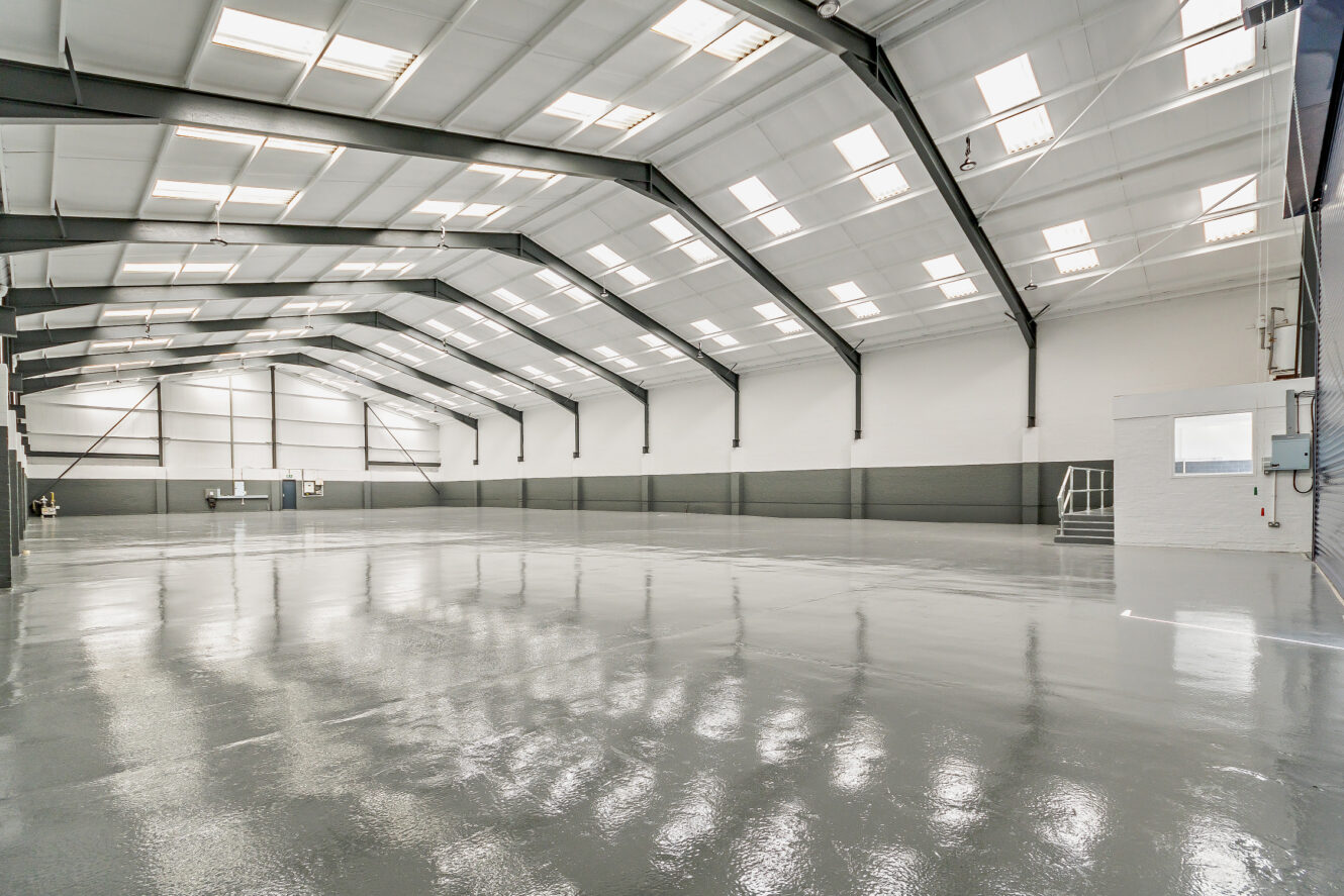 Interior view of a large, empty warehouse with polished concrete floors, high ceilings, and overhead lighting.