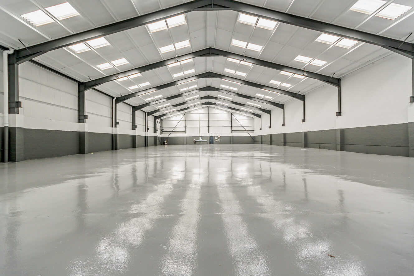 Interior of an empty warehouse with polished concrete floor, high ceiling, skylights, and exposed steel beams.