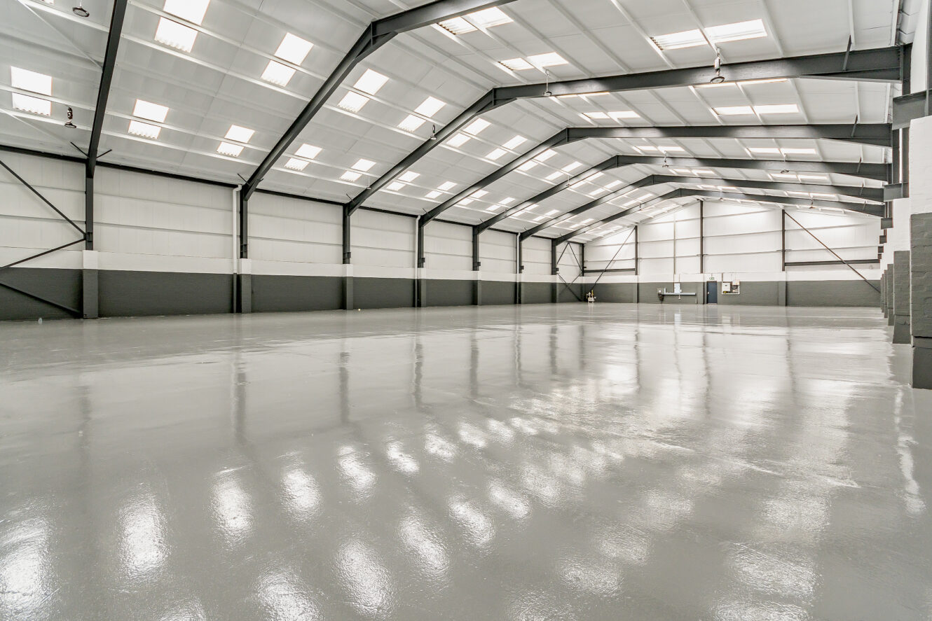 Large, empty industrial warehouse with high ceilings, white walls, black steel beams, and a shiny gray polished concrete floor.