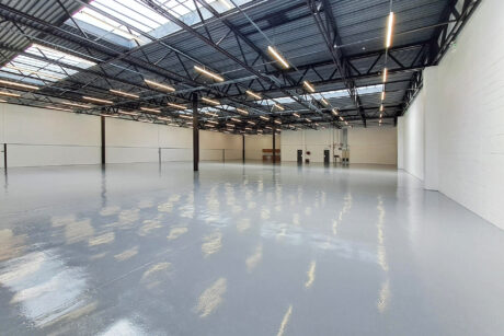Spacious, empty warehouse with polished concrete floor, white walls, high ceiling, and skylights allowing natural light inside.