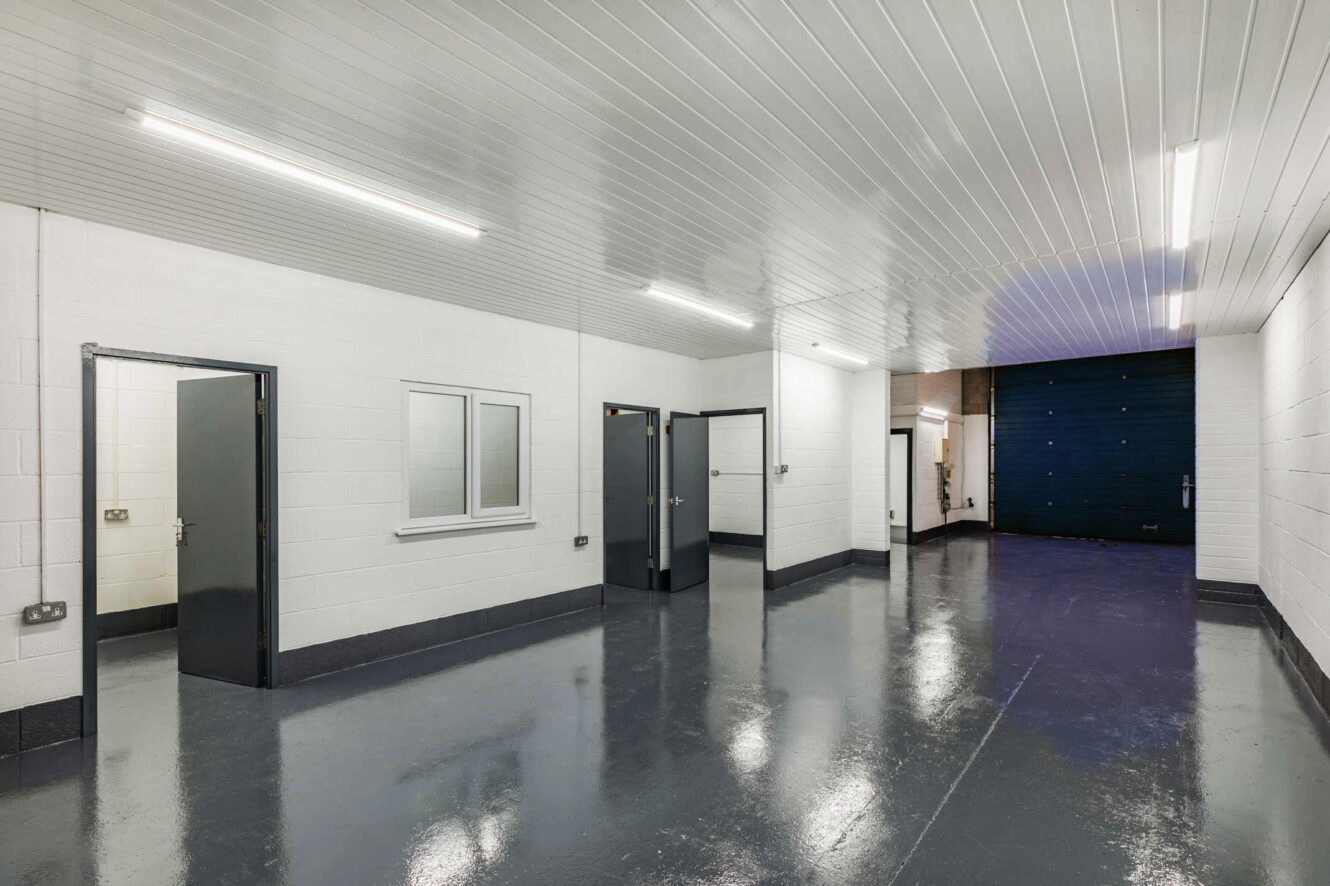 Industrial interior with white-painted brick walls, a shiny grey floor, several doors, a window, and overhead fluorescent lighting.
