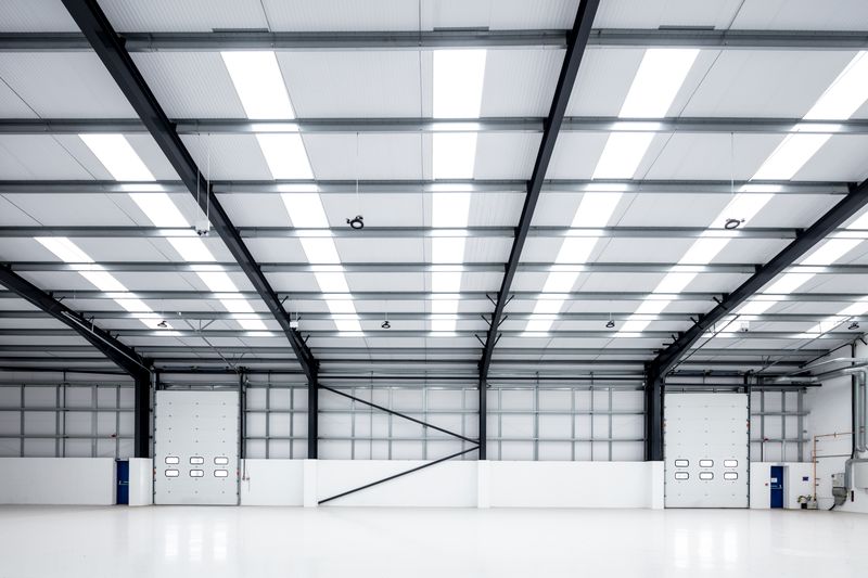 Interior of a large, empty, modern industrial warehouse with high ceilings, bright overhead lighting, and two large garage doors.