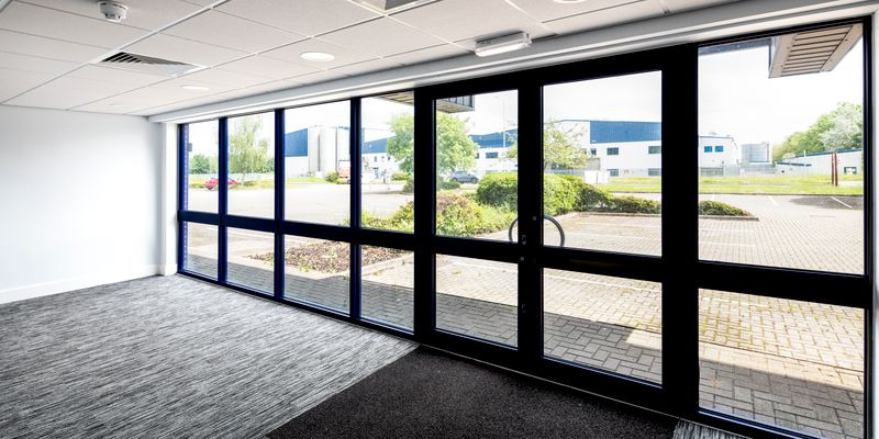 Office lobby with large floor-to-ceiling windows, offering a clear view of a parking lot and industrial buildings outside.