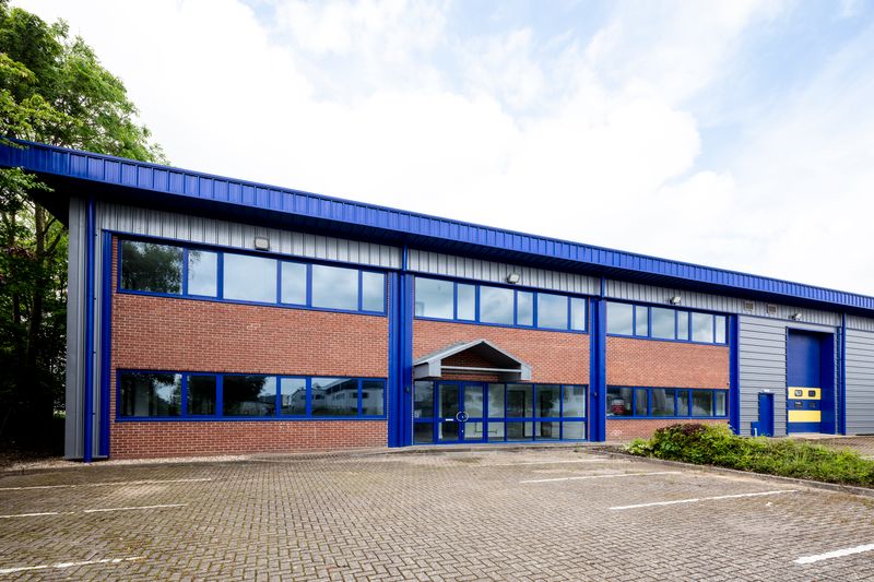 Modern industrial building with blue and red brick exterior, large windows, and empty parking spaces in front.