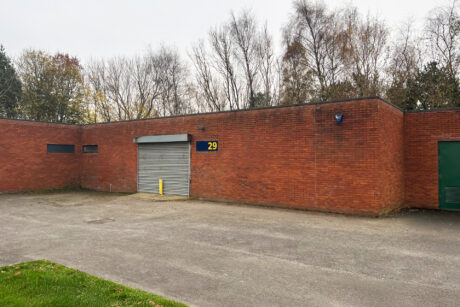 A brick building with a closed silver roll-up door labeled 29, surrounded by leafless trees and a paved area in front.