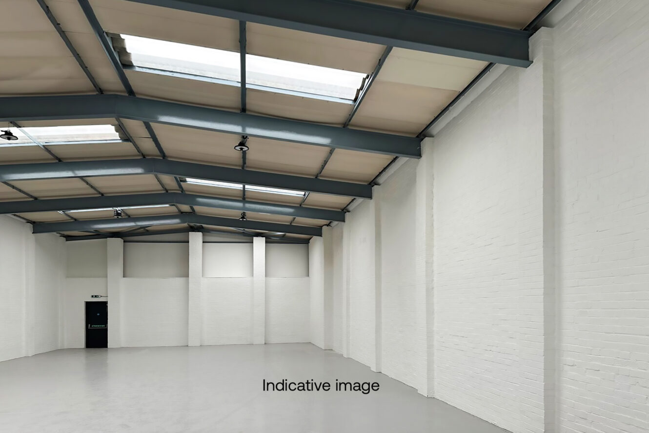 Empty industrial warehouse with white brick walls, grey concrete floor, metal beams, and skylights in the ceiling. The words Indicative image appear on the floor.