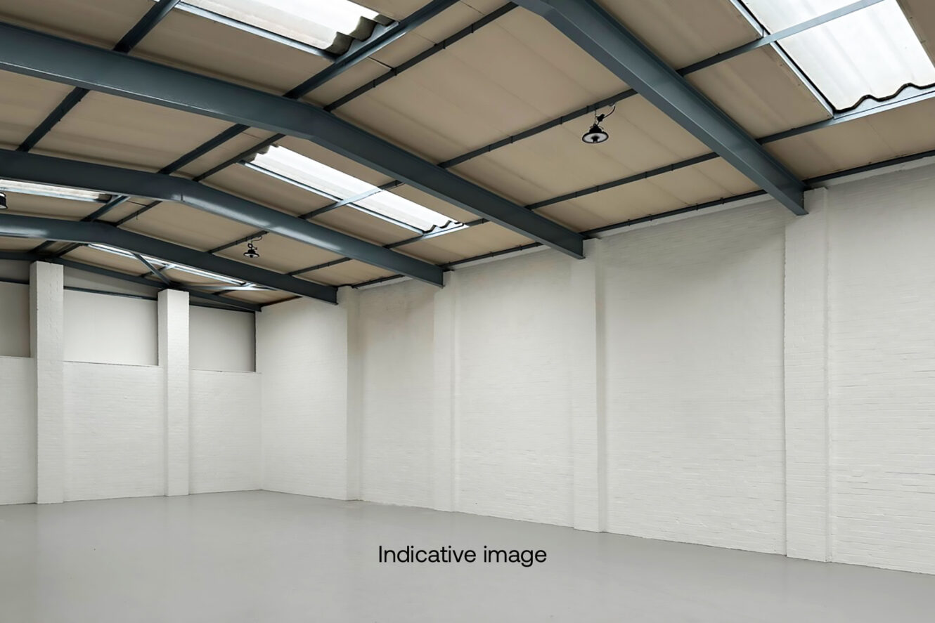Empty industrial warehouse with white brick walls, concrete floor, exposed metal beams, and skylights in the ceiling. The words Indicative image are on the floor.