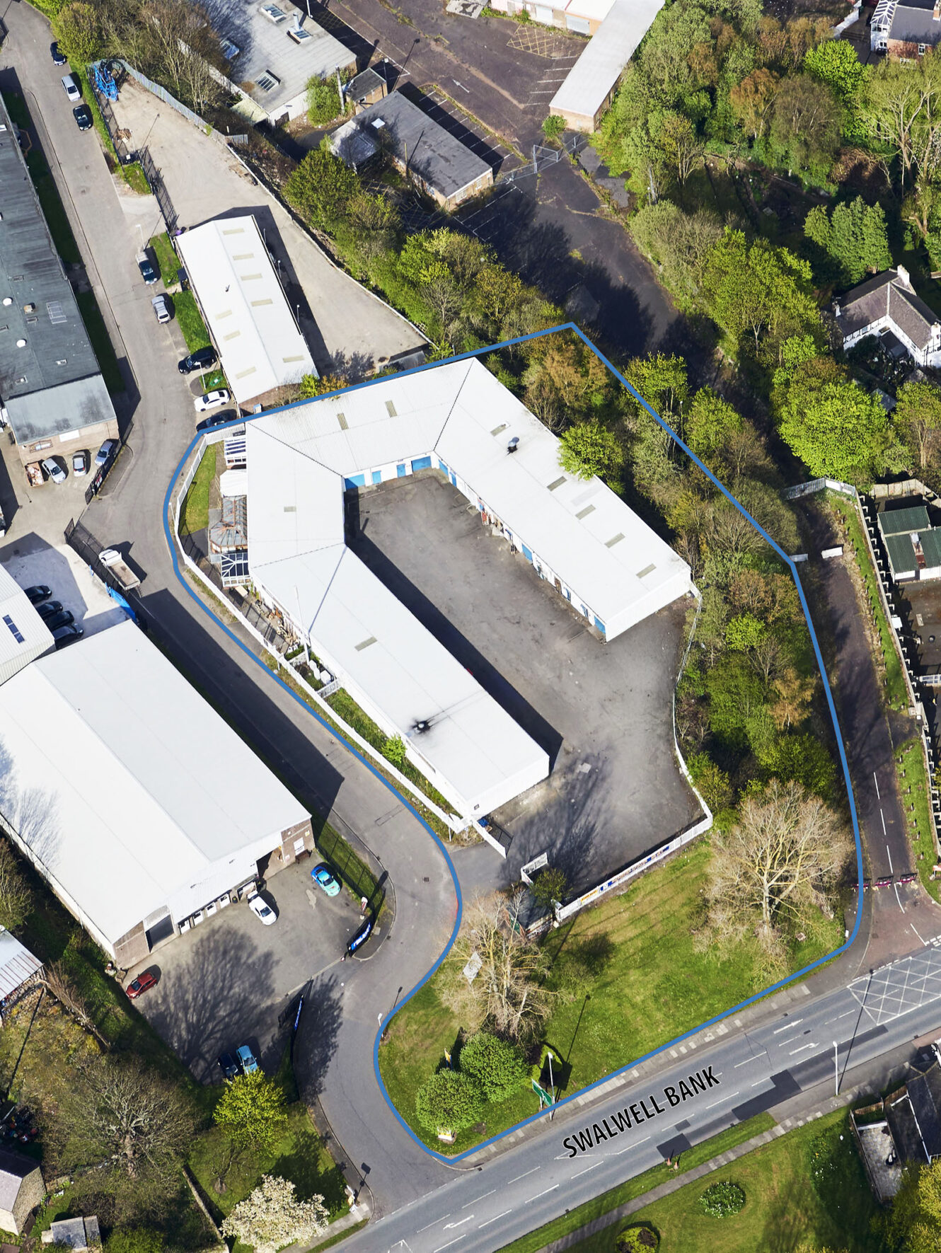 Aerial view of an industrial complex bordered by a blue outline, surrounded by trees, parking areas, and adjacent to Swalwell Bank road.