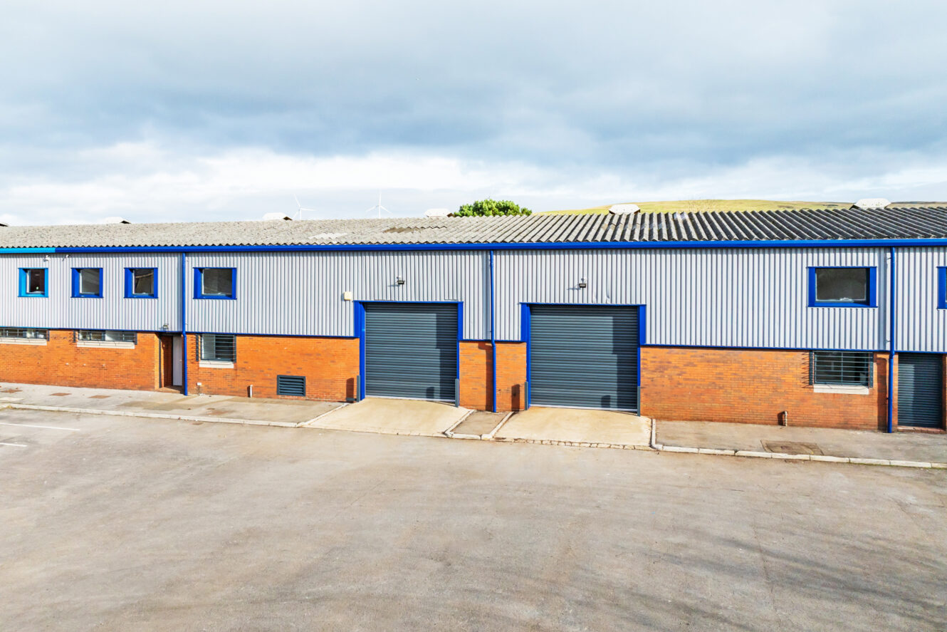 Exterior view of a commercial warehouse building with brick and metal siding, featuring two large blue roller doors and several windows.