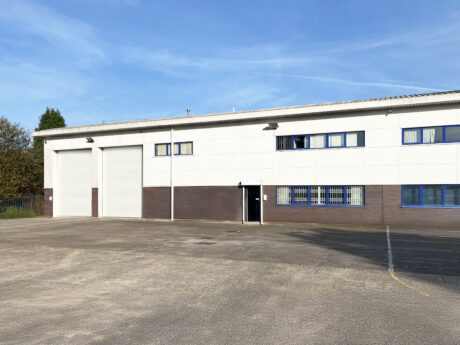A modern industrial warehouse building with two large garage doors, white and brown exterior, and an empty parking lot in front.