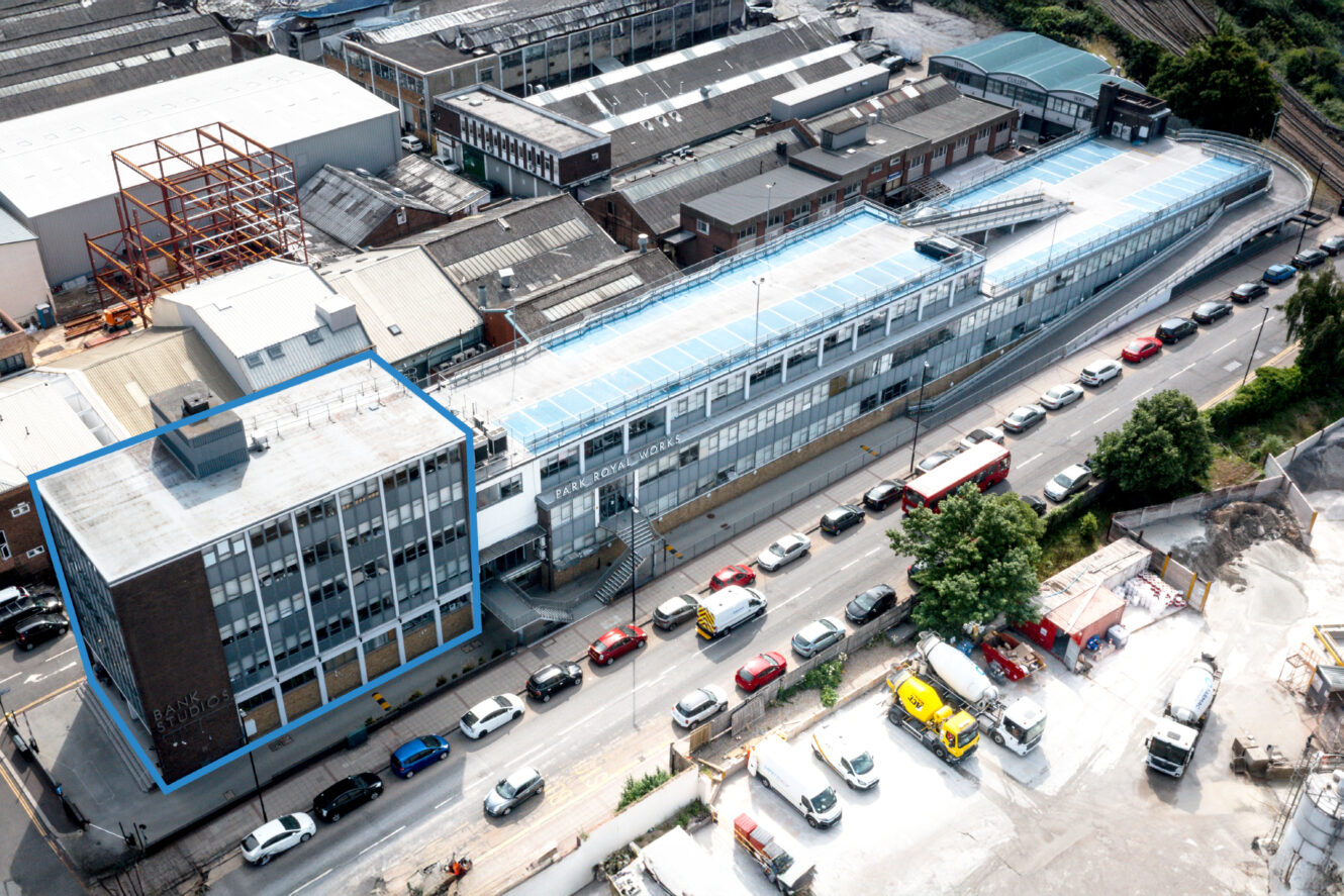 Aerial view of an industrial area with multi-story buildings, cars parked along the street, and construction materials in the foreground.