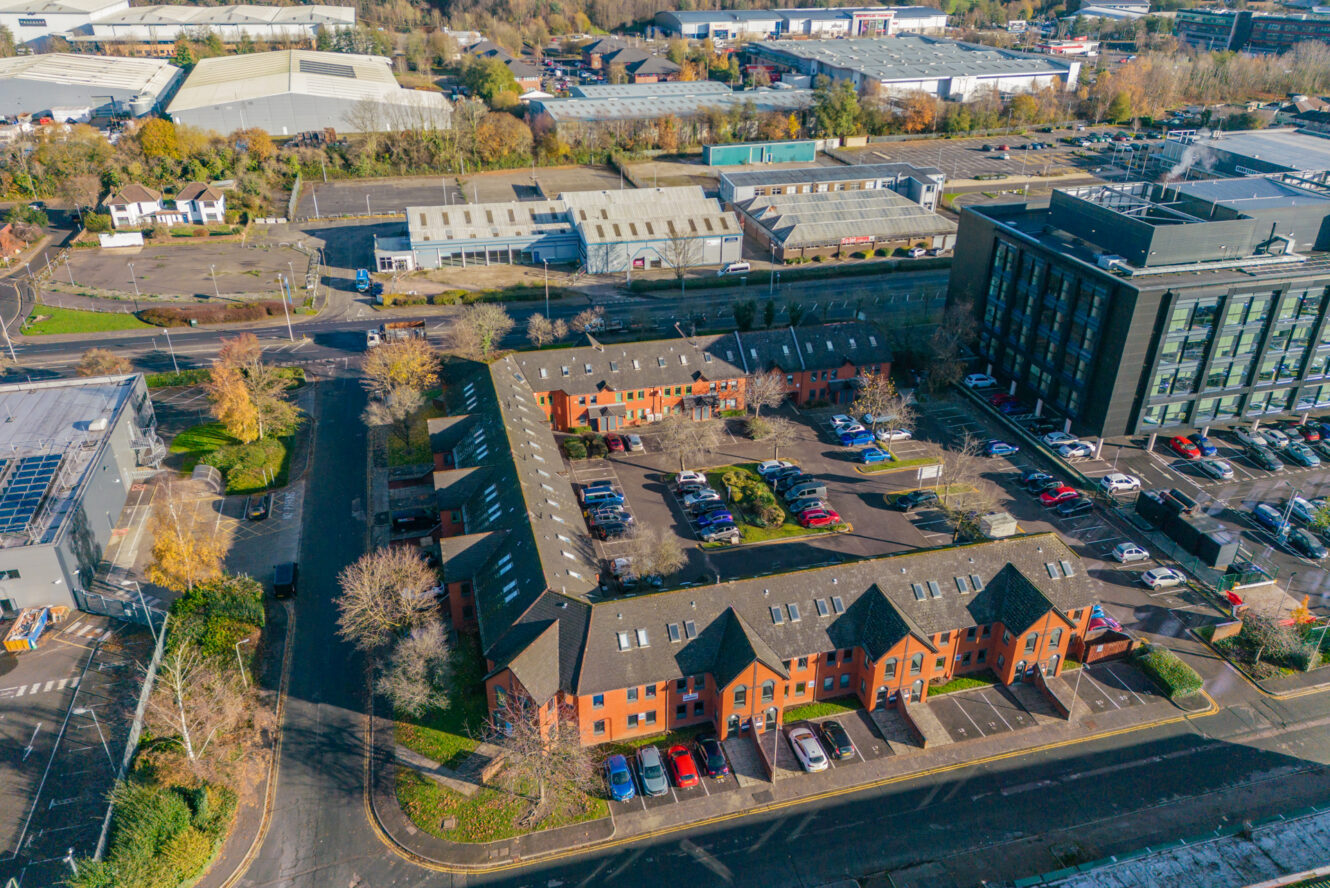Aerial view of office buildings, a parking lot with cars, and surrounding roads in an industrial and commercial area.