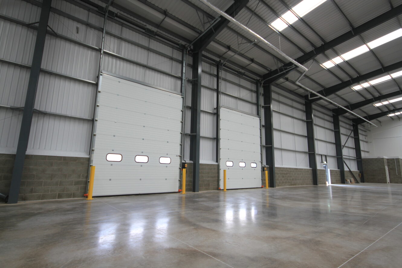 Interior of an empty warehouse with polished concrete floors, high ceilings, and two large closed industrial garage doors.