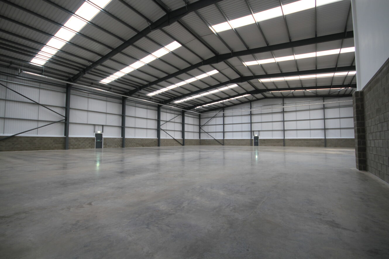 Interior of a large, empty warehouse with high ceilings, concrete floor, and multiple doors along the walls.