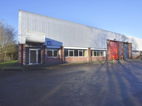 Industrial warehouse building with brick and metal exterior, large red loading door, windows, and entry door under a blue sign labeled A3 on a clear day.