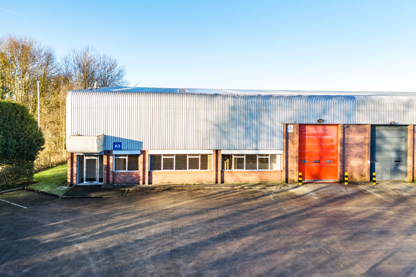 Single-story industrial building with corrugated metal roof, red and gray loading bay doors, multiple windows, and a small entrance labeled A3.