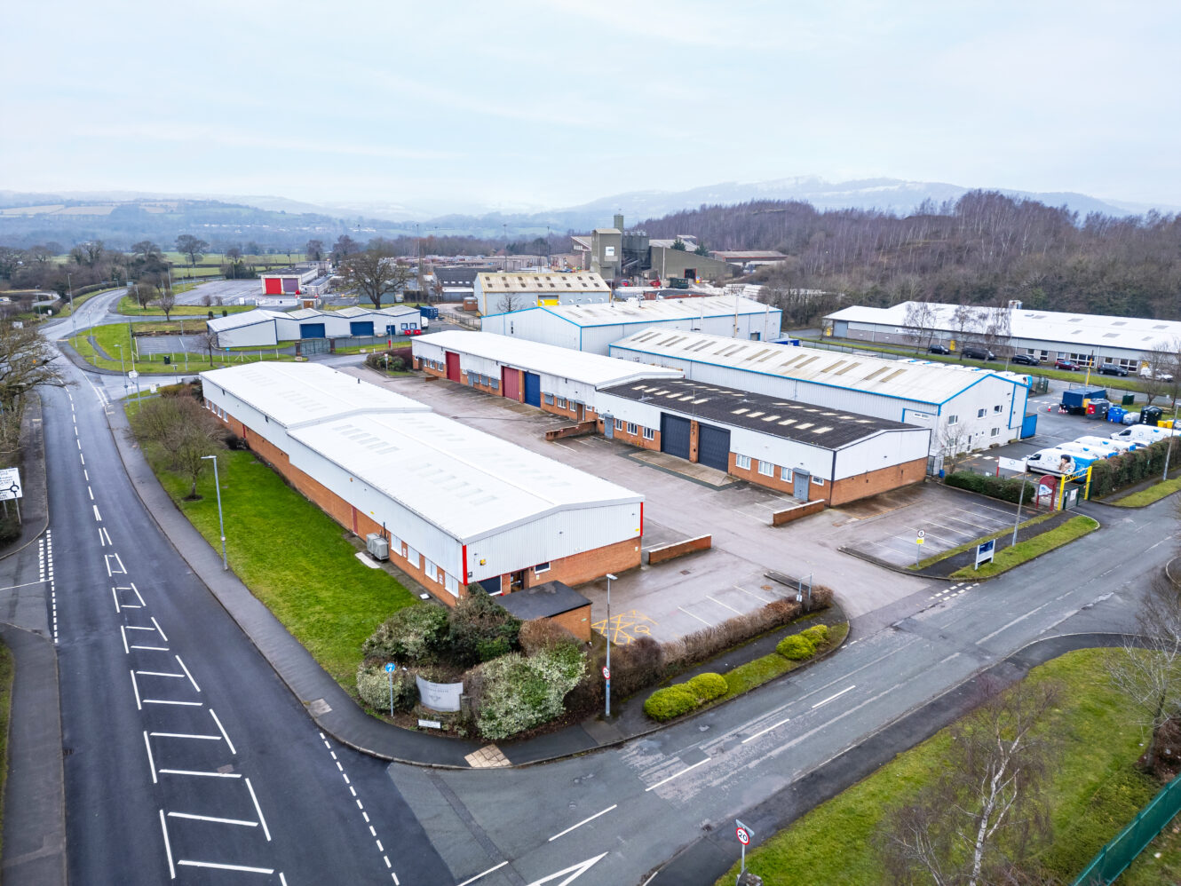 Aerial view of an industrial park with several large warehouse buildings, parking areas, and surrounding roads in a semi-rural setting.