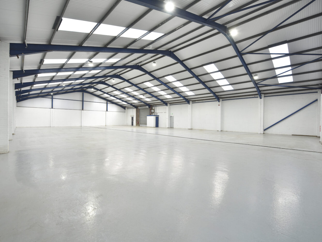 Spacious, empty warehouse interior with a polished concrete floor, white walls, high ceiling, and skylights allowing natural light into the space.