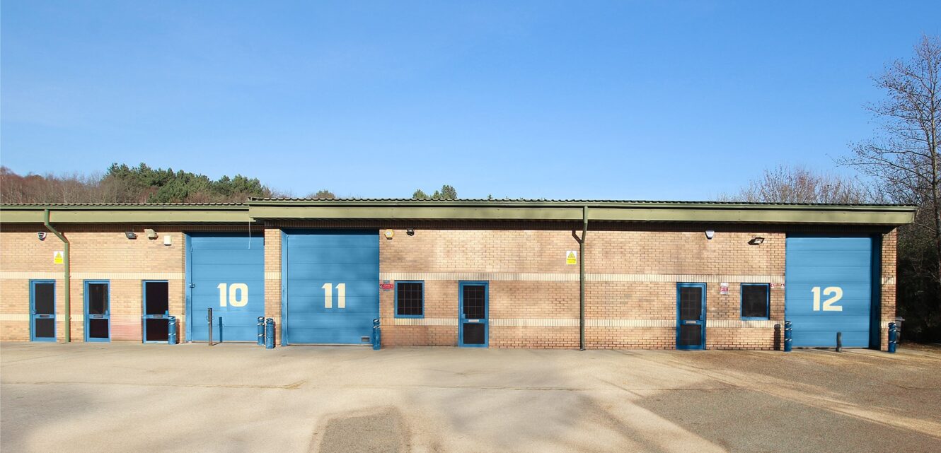 A row of three industrial warehouse units with blue doors numbered 10, 11, and 12, under a clear blue sky.