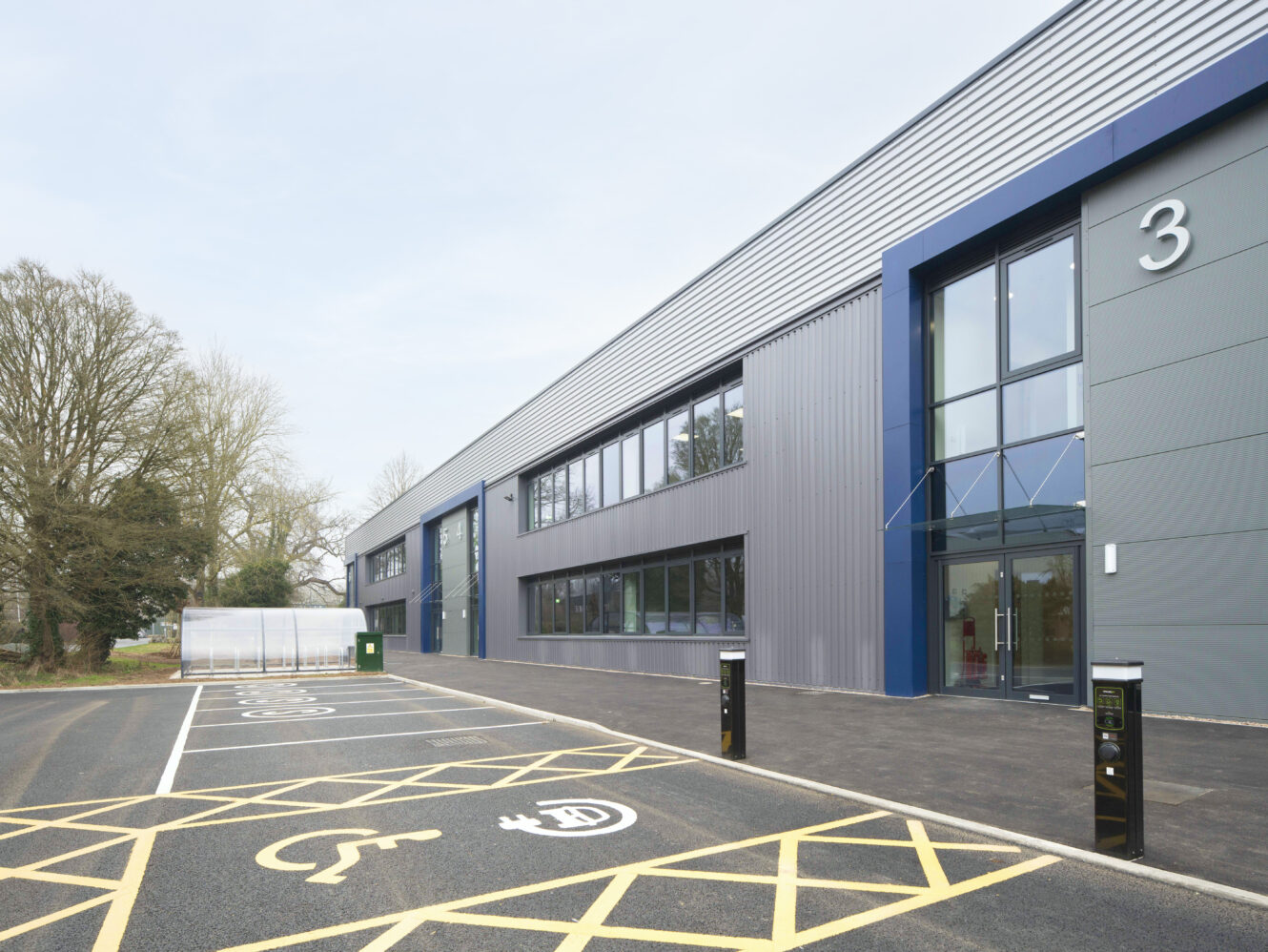 Accessible parking spaces and electric vehicle charging points in front of a modern industrial or office building with large windows and a glass entrance.