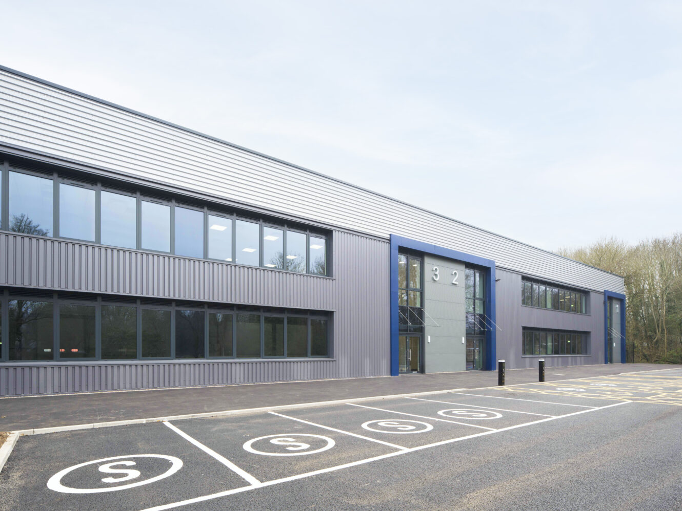 Modern two-story industrial or office building with large windows and designated parking spaces labeled S in front.