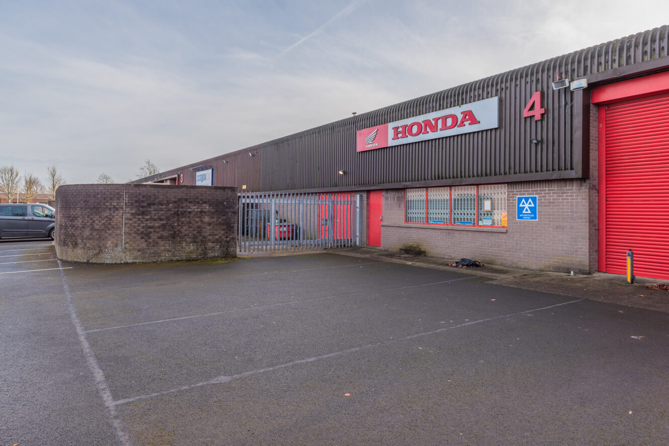Exterior of a Honda service center with red doors, a large sign, and a gated entrance, located in an industrial-style building marked with the number 4.