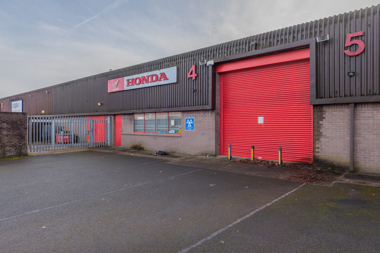 A Honda industrial unit with a red roller shutter door, labeled as unit 4, next to unit 5, and displaying an MOT test sign in a mostly empty parking lot.