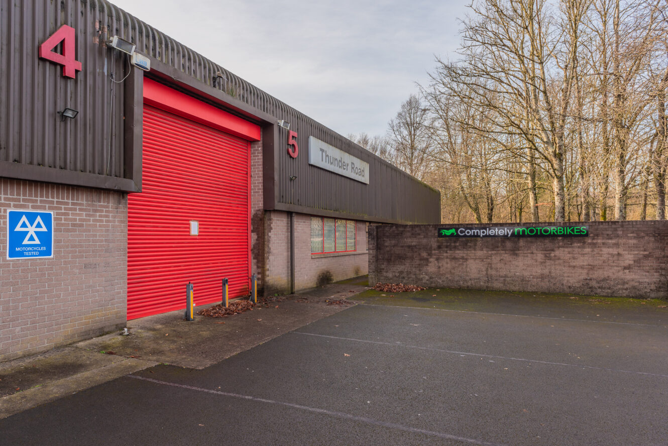 Warehouse building with red garage door labeled units 4 and 5, with Thunder Road sign and Completely Motorbikes sign on adjacent brick wall.