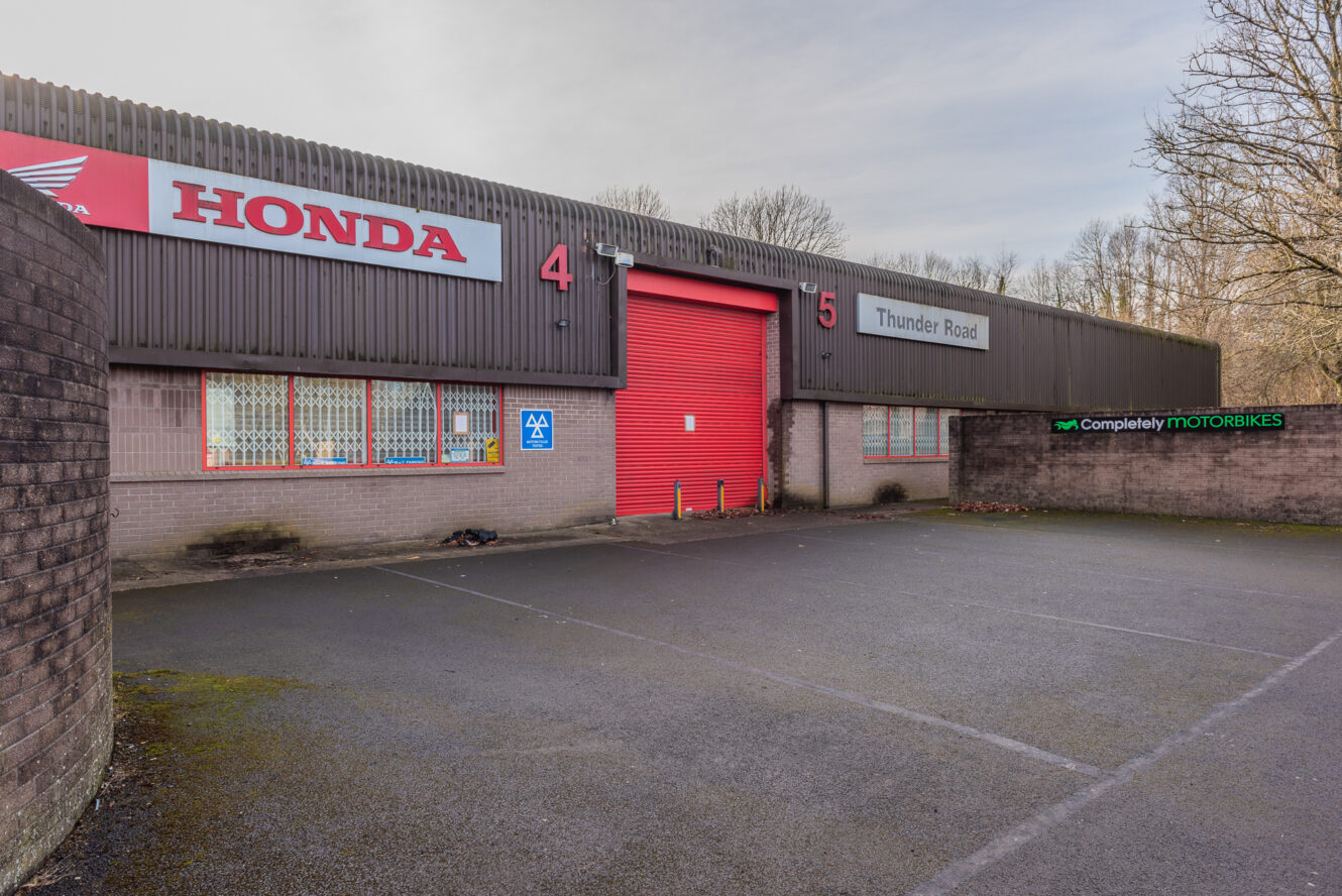 A Honda dealership with red doors, labeled units 4 and 5, Thunder Road signage, and a Completely Motorbikes sign, viewed from an empty parking lot.