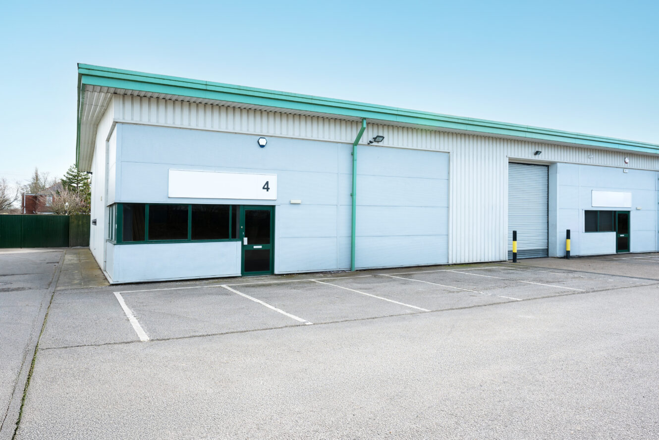 A modern industrial unit with large windows, a roller shutter door, and empty parking spaces in front, labeled with the number 4.