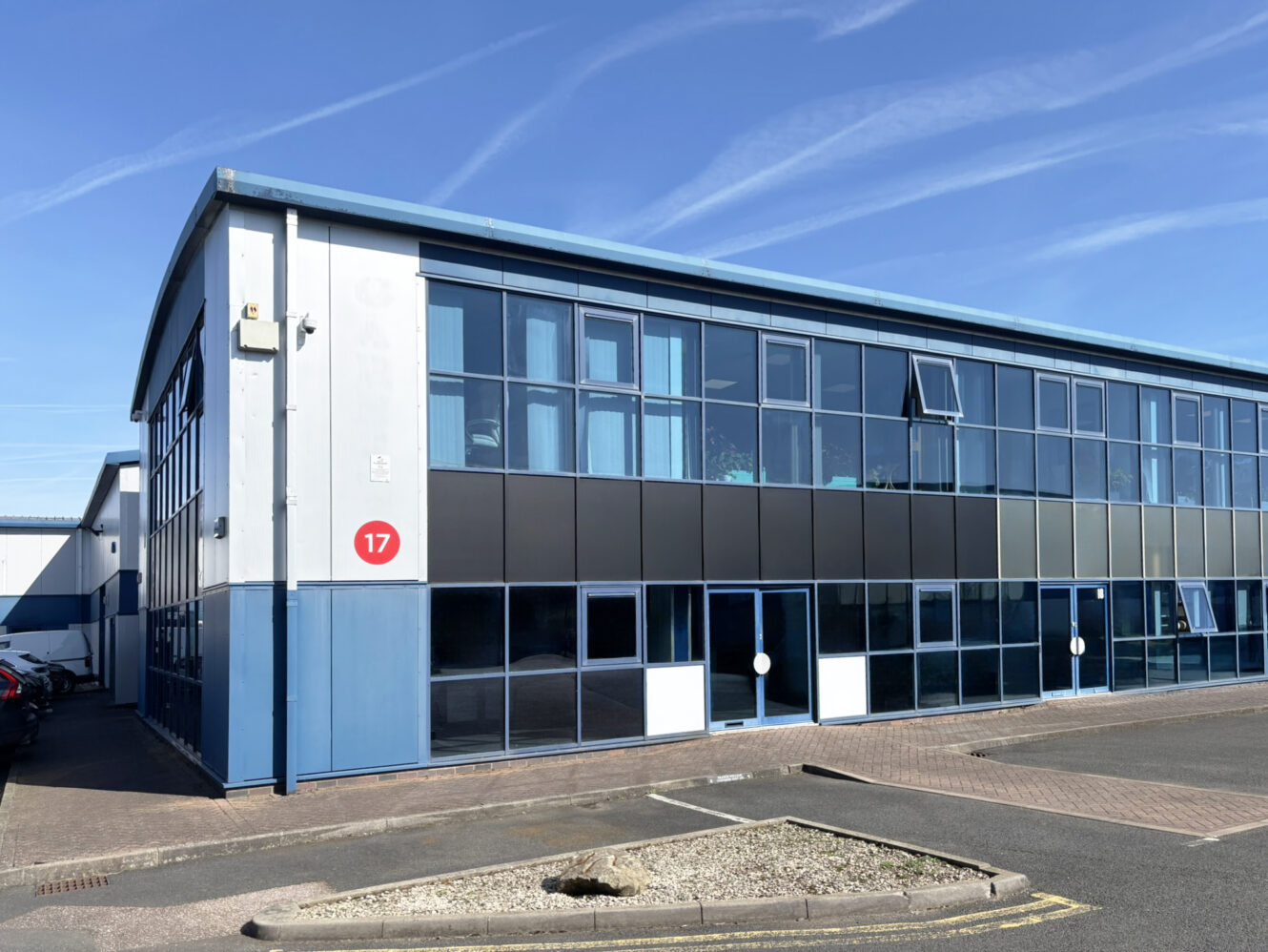 A modern, two-story commercial office building with large glass windows, marked with the number 17, under a clear blue sky.
