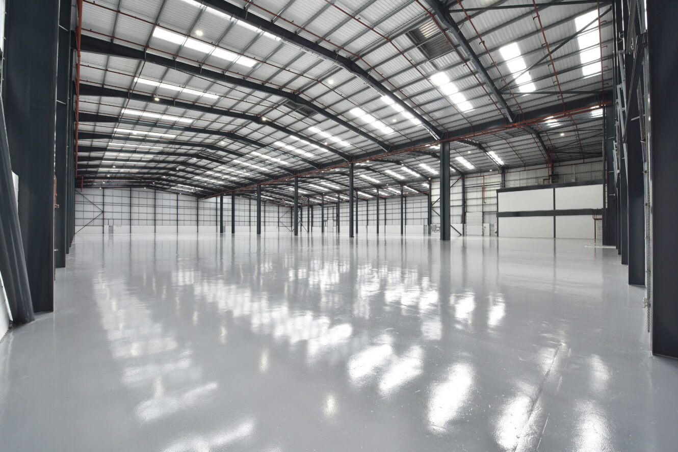 Interior of a large, empty warehouse with polished concrete floors, high ceilings, metal beams, and bright overhead lighting.