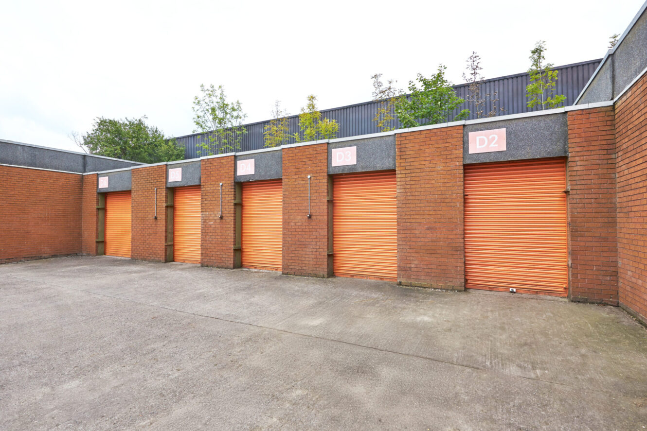 Row of orange storage unit doors with labels D1 to D5, set in a brick building, viewed from a paved outdoor area.