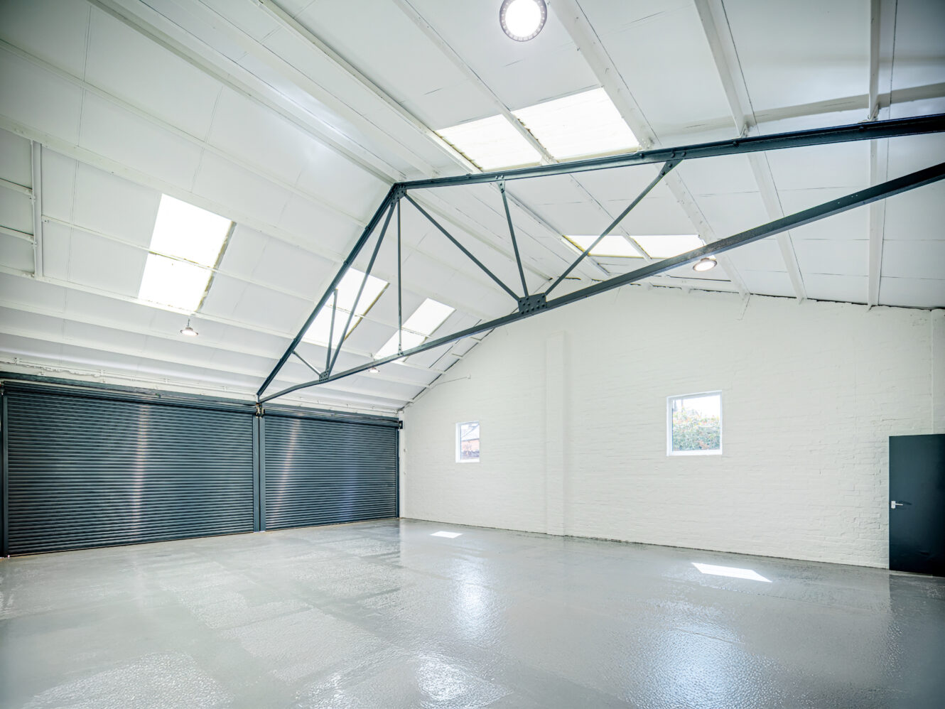 Spacious empty warehouse with white walls, polished concrete floor, large roller doors, high ceiling, and skylights letting in natural light.