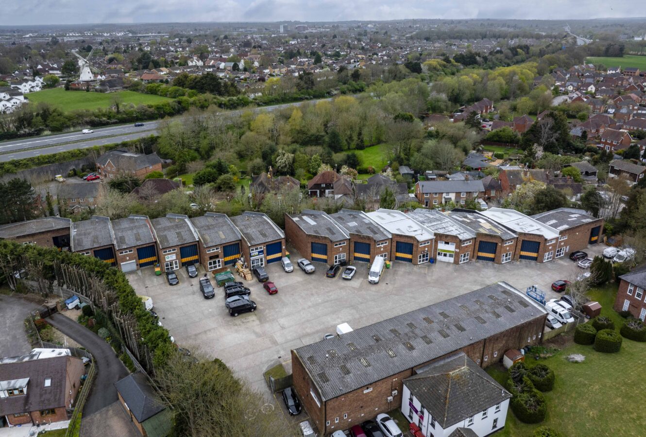 Aerial view of a commercial business park with multiple units, parked vehicles, and surrounding residential areas and greenery.