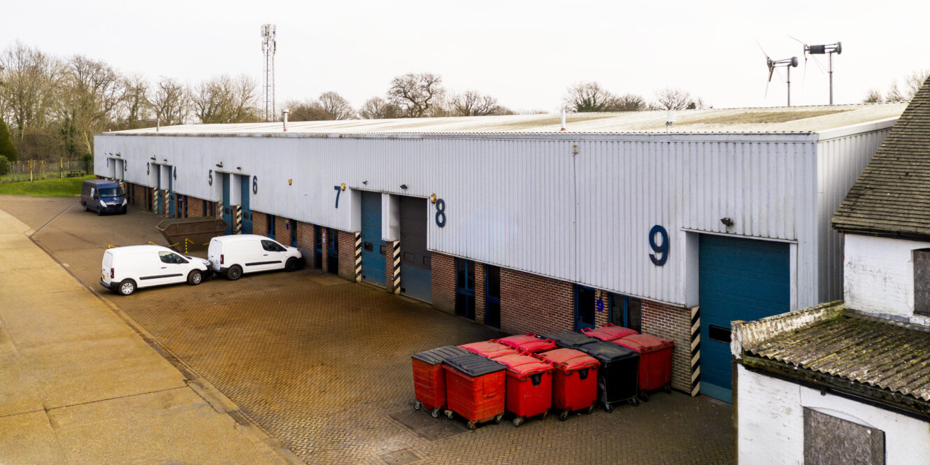 A row of industrial warehouse units with blue doors, labeled 7 to 9, two white vans parked outside, and several red carts lined up near door 9.