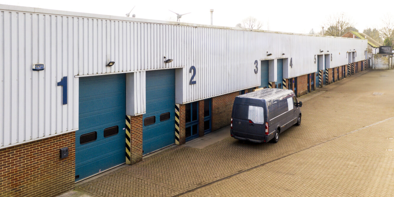 A black van is parked outside a row of blue industrial loading bay doors numbered 1 to 4 on a brick and metal building.