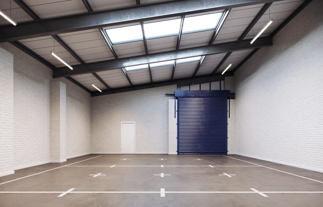 Empty warehouse interior with white brick walls, a high ceiling with skylights, a small white door, a large blue roller shutter door, and marked parking spaces on the concrete floor.