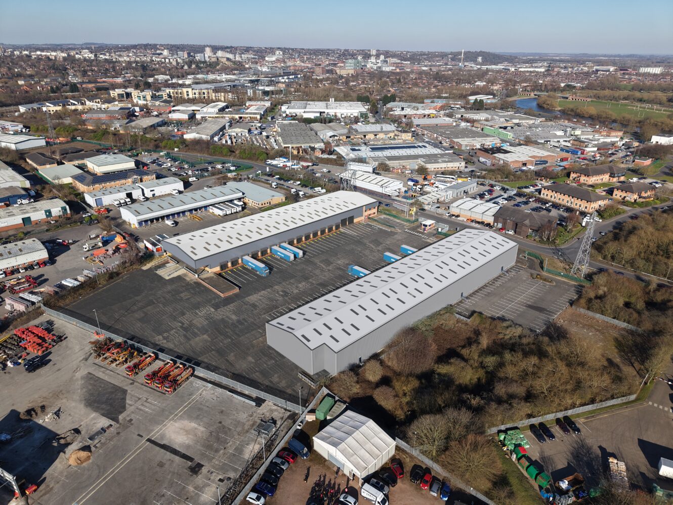 Aerial view of an industrial park with large warehouse buildings, parking lots, trucks, and surrounding urban infrastructure.