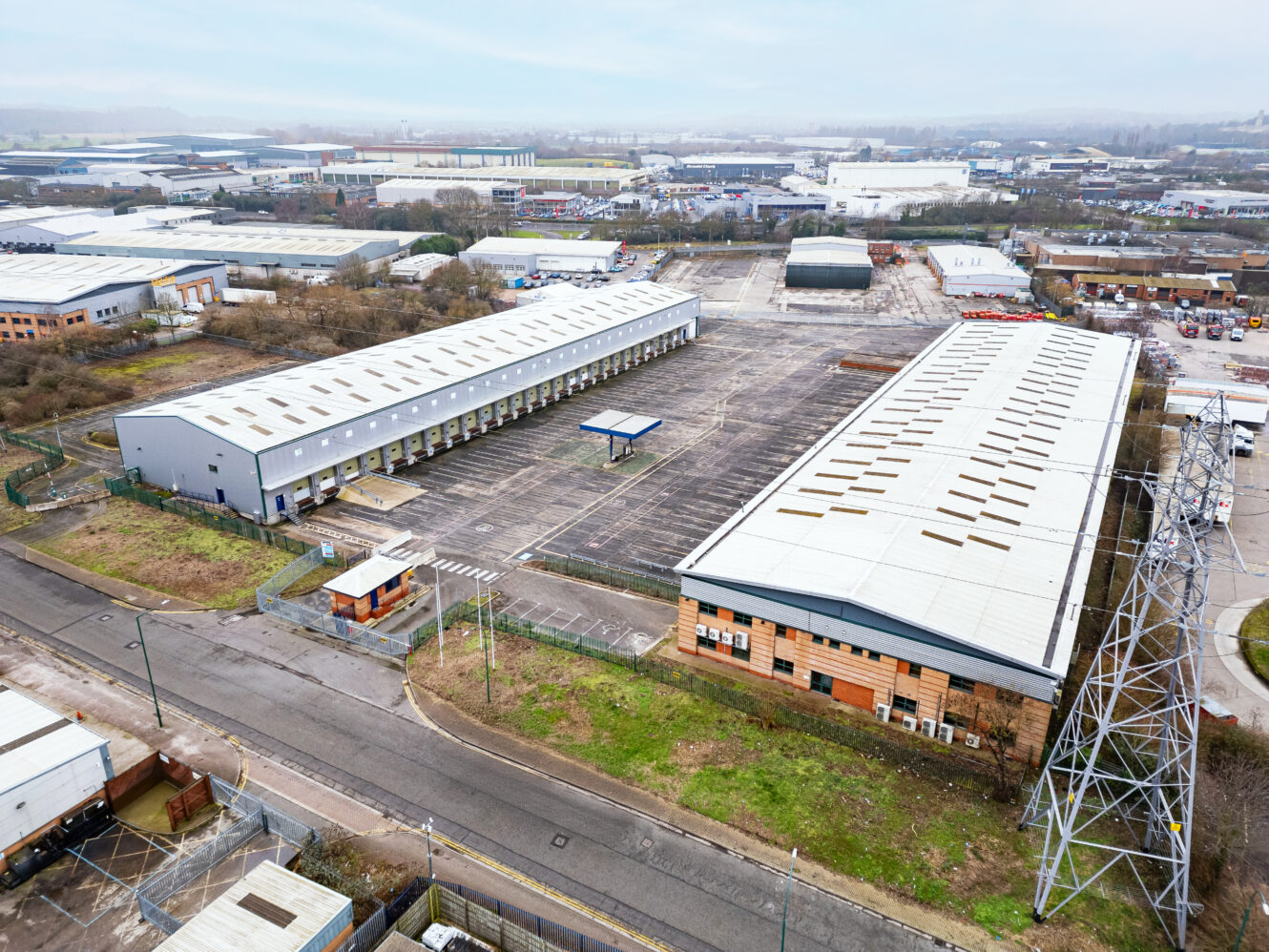 Aerial view of two large warehouse buildings with an adjacent parking area in an industrial estate.