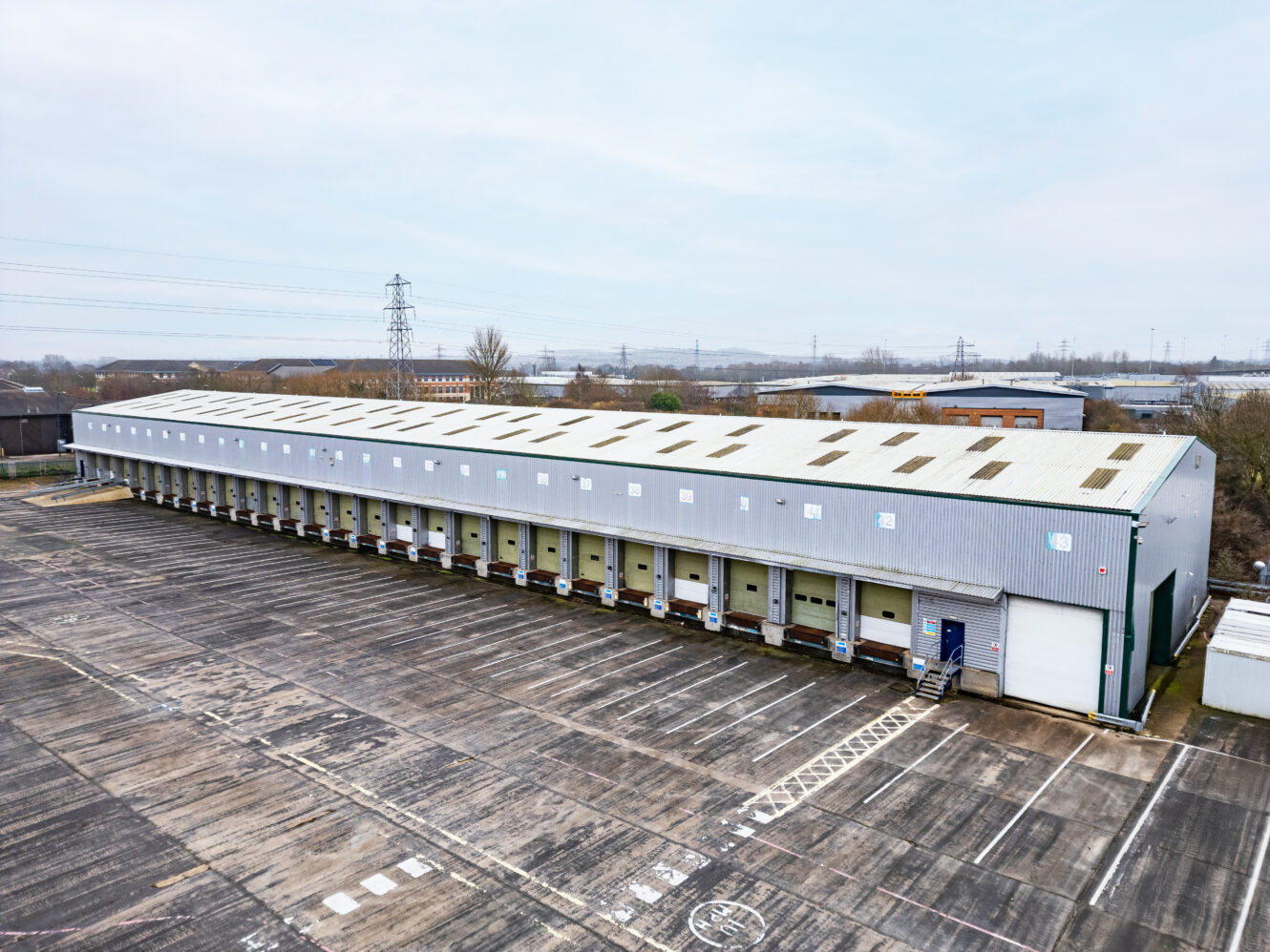 A large industrial warehouse with multiple loading docks and an empty parking lot, photographed from an elevated angle.
