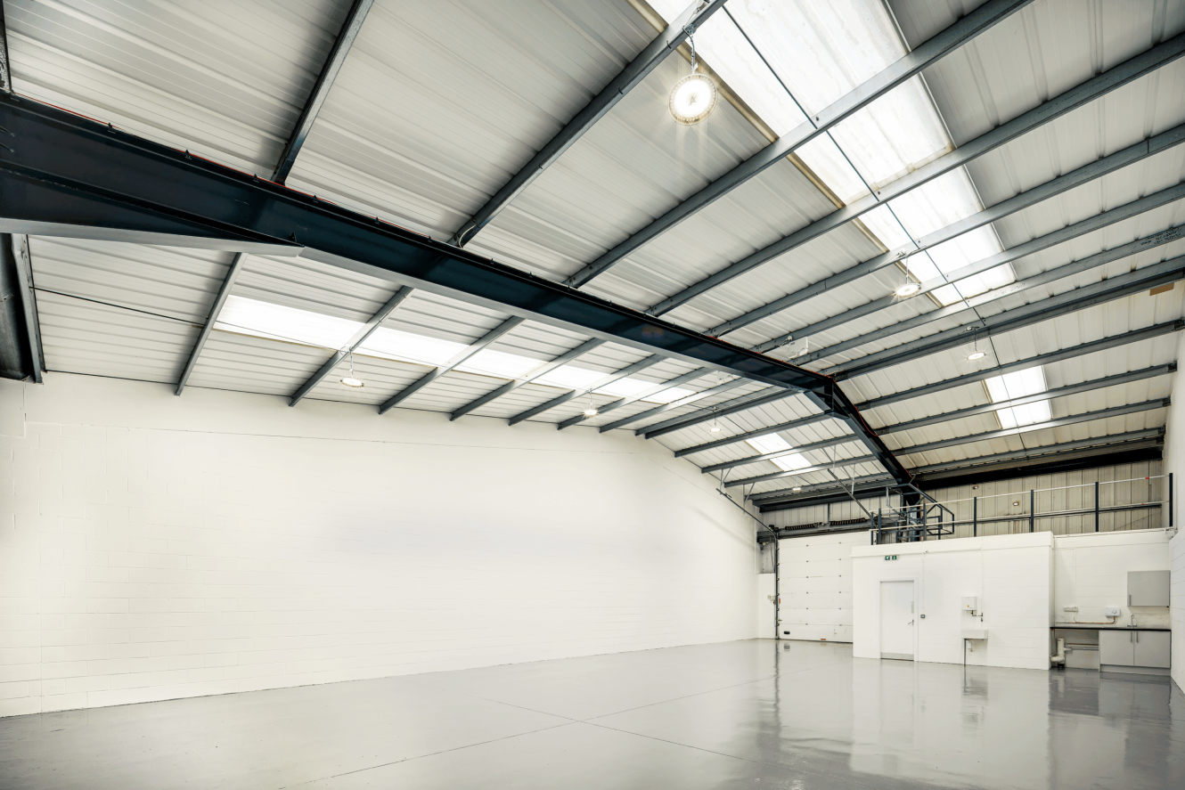 Empty industrial warehouse interior with a polished concrete floor, white painted brick walls, and a high metal ceiling with skylights and exposed beams.