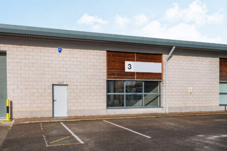A modern industrial building with a sign labeled 3, a single door, large windows, and an empty parking lot in front.