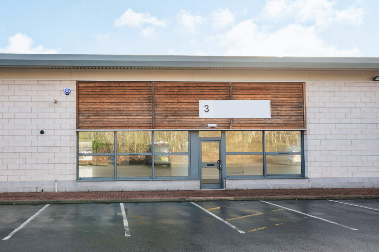 A modern, single-story commercial building with large windows, a door in the center, an empty sign above marked 3, and an empty parking lot in front.