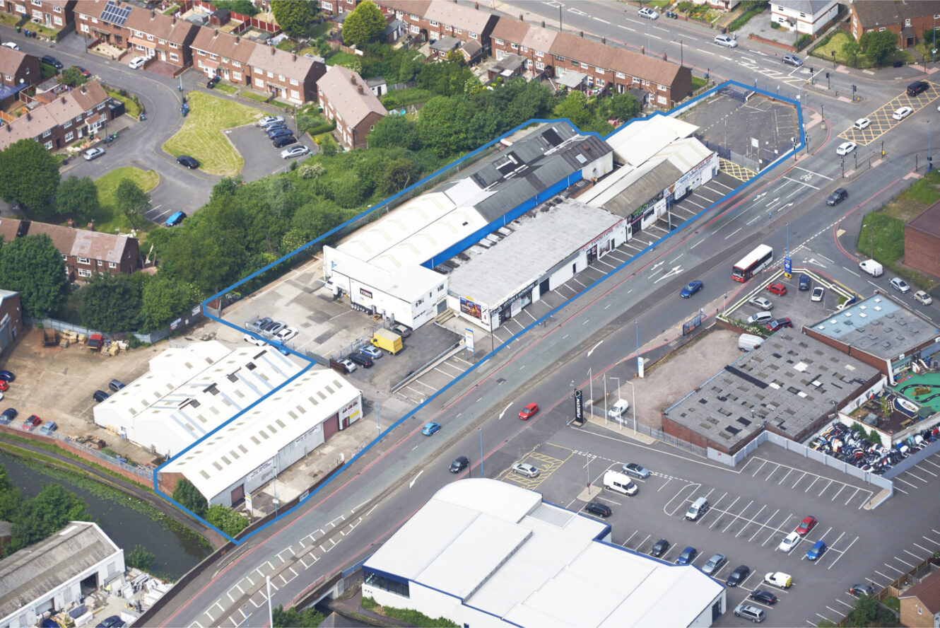 Aerial view of an industrial and commercial area with warehouses, parking lots, and nearby residential housing. A blue outline marks the boundary of a specific property.