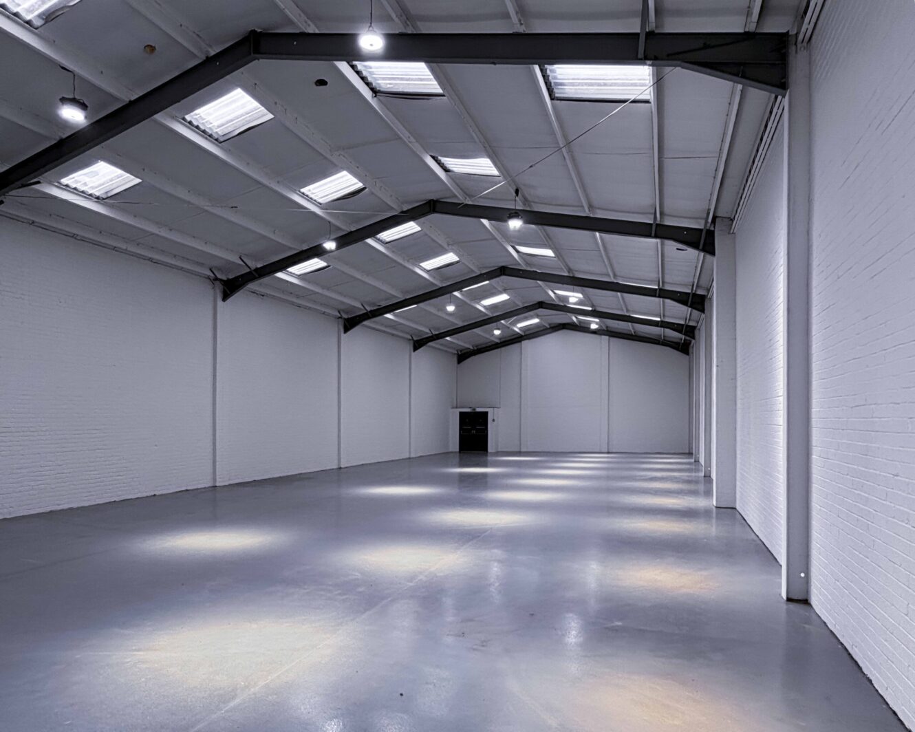A large, empty industrial warehouse with white walls, high ceilings, exposed beams, and skylights letting in natural light.